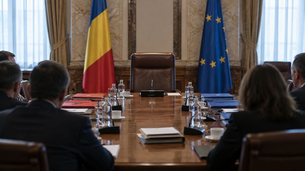 Masă de negocieri politice cu un loc central liber și drapelele României și Uniunii Europene